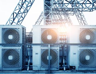 Air conditioner units (HVAC) on a roof of industrial building with blue sky and clouds in the background.